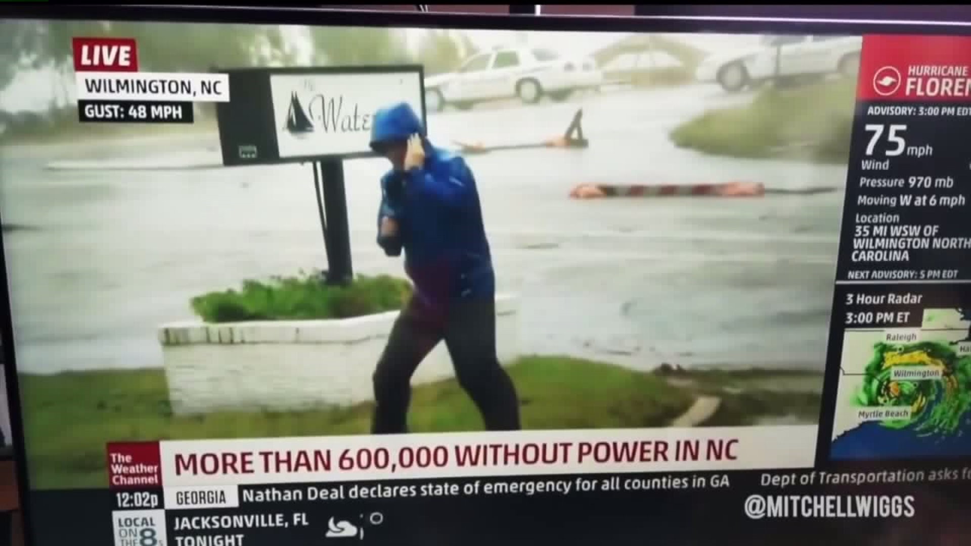 Meteorologist braces against wind while 2 men stroll by