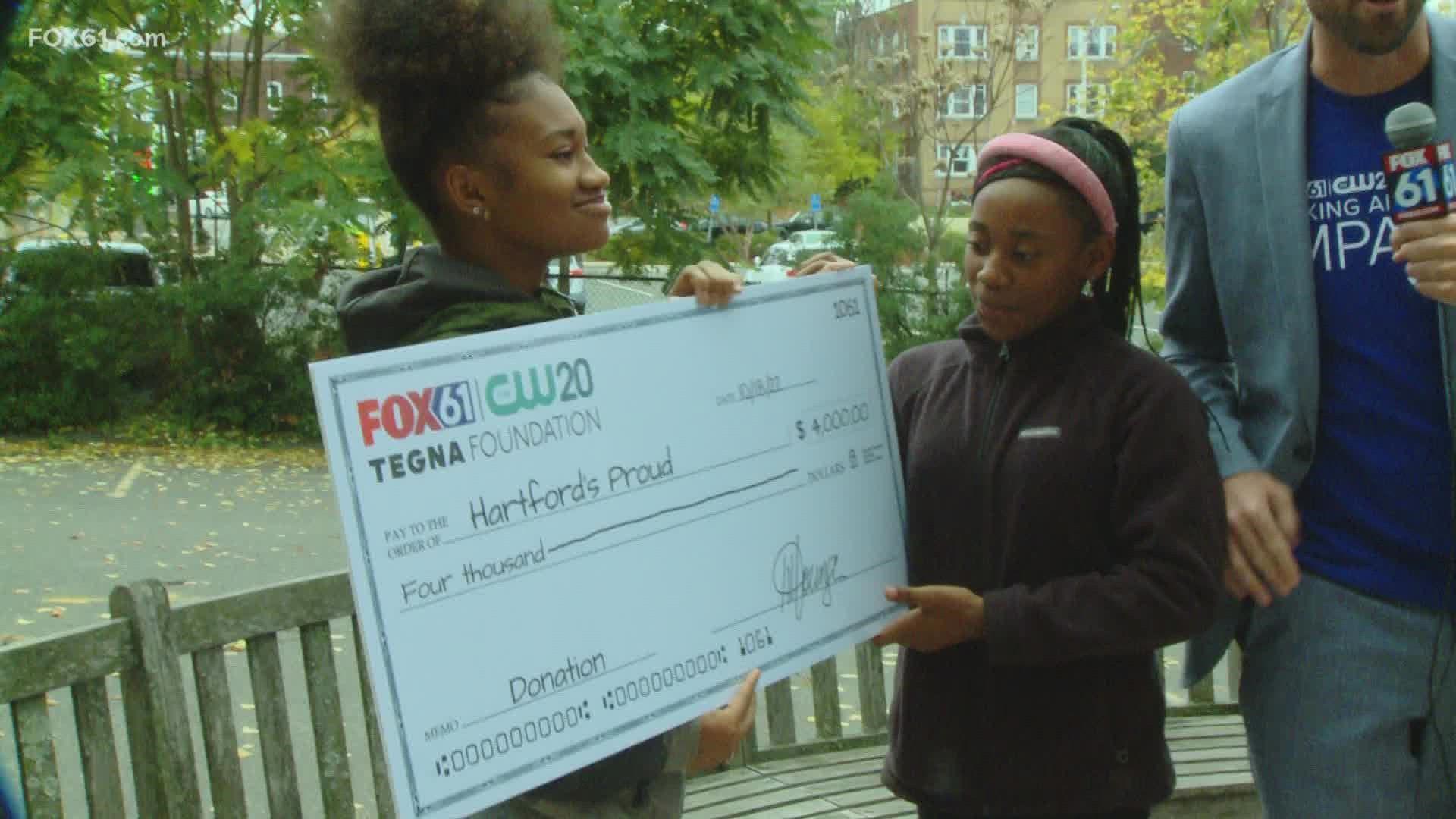 FOX61 and TEGNA presents the nonprofit organization Hartford’s Proud Drill, Drum, and Dance Corporation with a check.